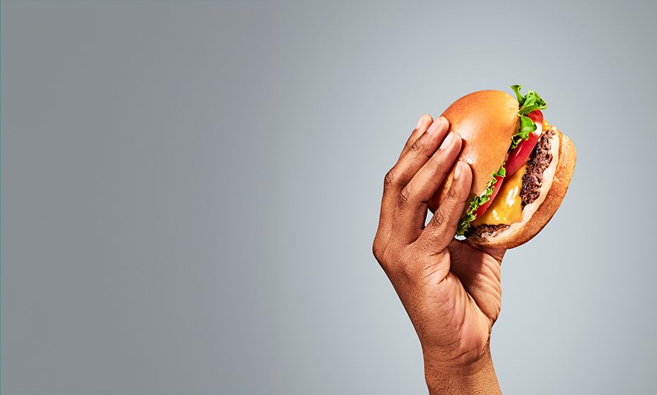 A hand holding a cheese burger representing the quick-service hospitality industry